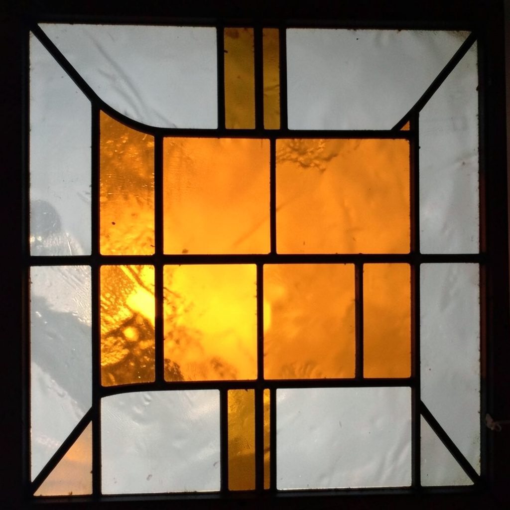 Stained-glass composition in pale grey and warm amber, square panels