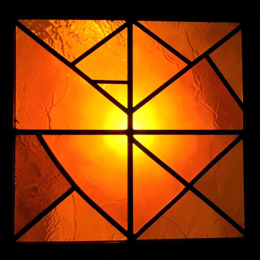 Abstract painterly composition in deep amber and terracotta tones with bold leaded segments, evoking a stained-glass atmosphere.